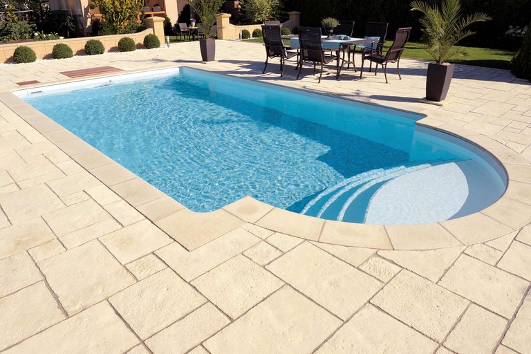 Schwimmbad mit hellen Steinplatten und Sitzbereich im Garten