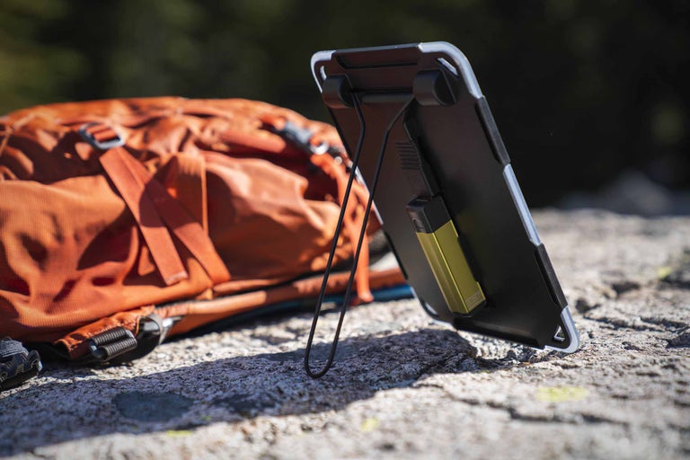 Smartphone mit Outdoorhülle und Rucksack auf einem Stein