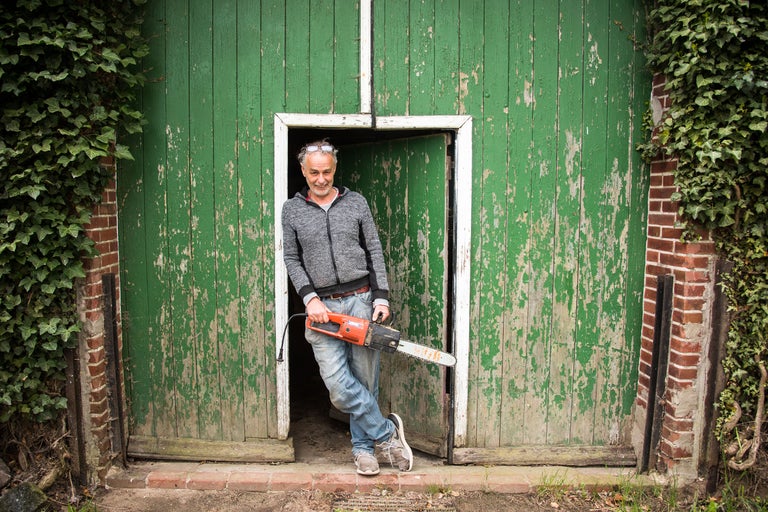 Mann mit elektrischer Kettensäge vor einer grünen Holztür