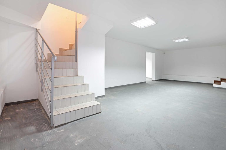 Heller Kellerraum mit Treppe, grauer Betonboden und Deckenleuchten