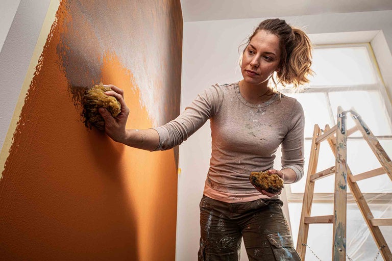Frau gestaltet Wand mit Schwamm und Farbe, inklusive Leiter im Raum