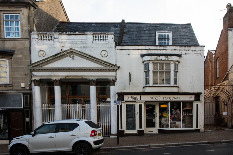 Gebäudeansicht mit den Hausnummern 15 und 16, in denen sich ein Strohhutladen und ein Teddybärgeschäft befinden