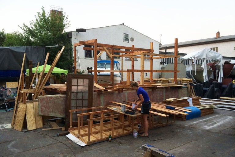 Szene einer Frau, die an einem Bauprojekt mit Holz arbeitet, mit Holzbalken, einem unfertigen Holzrahmen und Farbeimern in einer unordentlichen Umgebung