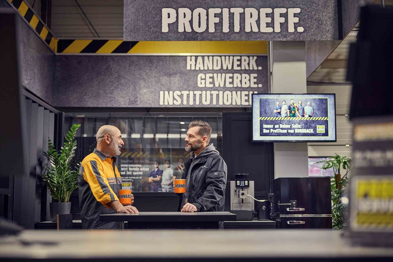 Zwei Männer stehen im Hornbach ProfiTreff mit Hornbach Tassen an einem Tisch.
