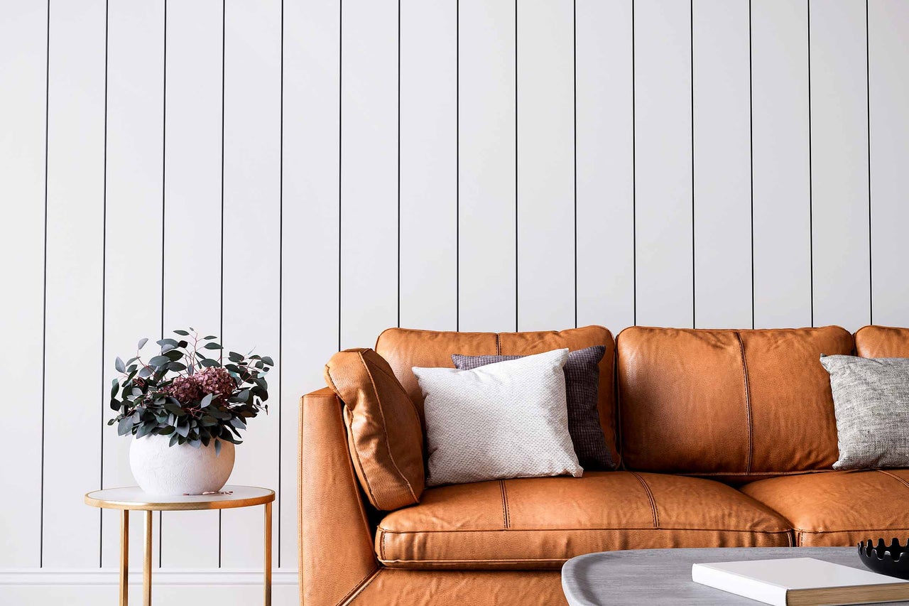Wohnzimmer mit braunem Ledersofa, Kissen, Beistelltisch mit Blumenvase und Paneelwand
