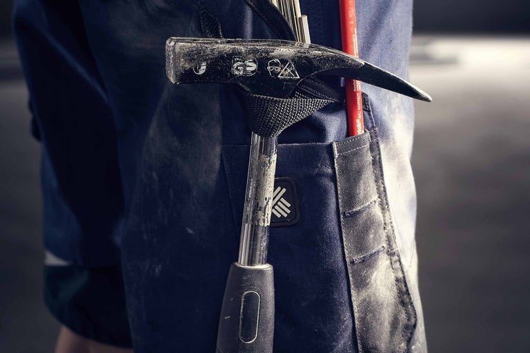 Detailaufnahme einer Arbeitshose mit Hammerhalterung, in der ein Hammer und ein Stift stecken.