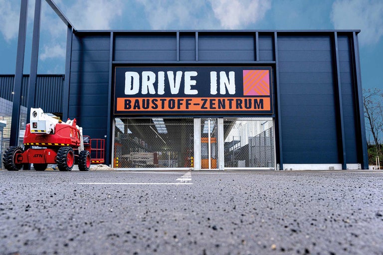 Außenansicht eines Drive-In Baumarktes mit Hubarbeitsbühne vor dem Eingang