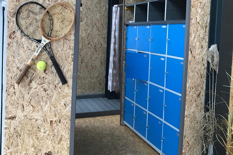 Innenraum mit blauen Schließfächern, Umkleidekabine mit Vorhang, zwei Tennisschlägern und einem Tennisball