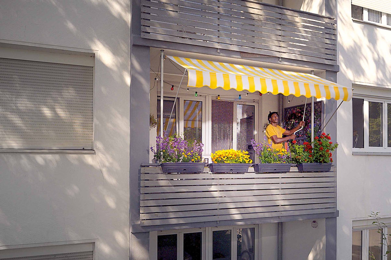 Mann kurbelt eine gelbe Markise auf dem Balkon aus.