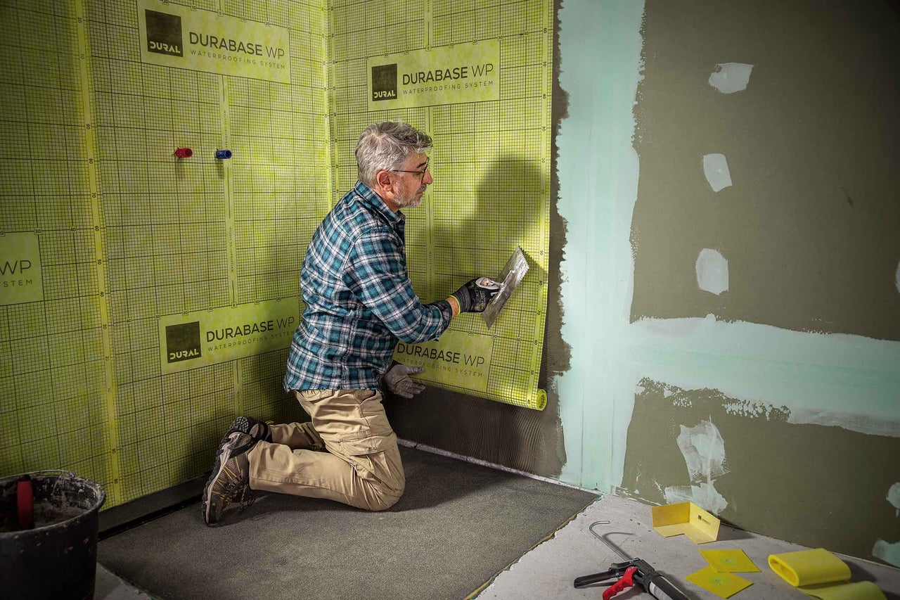 Ein Mann dichtet eine Wand im Innenbereich mit Dichtband ab, im Vordergrund Werkzeuge