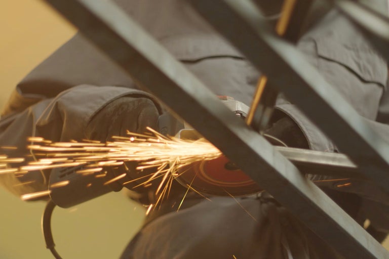 Ein Mann schleift Metall mit einem Winkelschleifer, wodurch Funken entstehen.