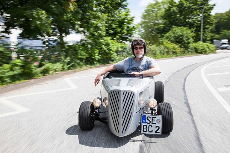 Mann fährt ein Hot Rod Fahrzeug auf einer Straße.