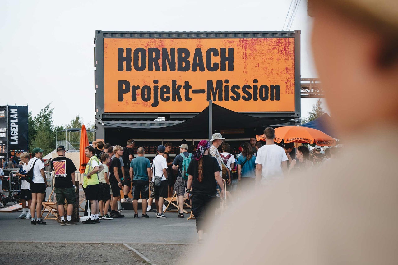 Ein Hornbach Informationsstand auf einem Festival mit einem Container und dem Schild Hornbach Projekt Mission sowie vielen Besuchern.