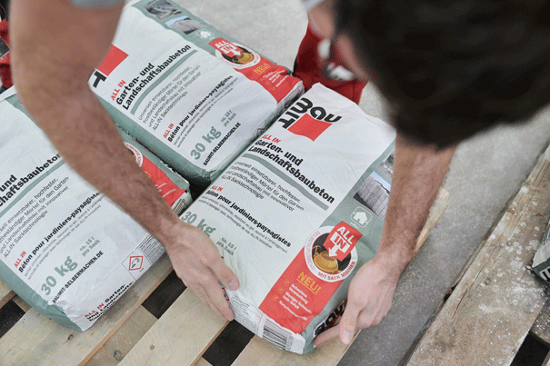 Person hantiert mit Säcken Garten- und Landschaftsbaubeton auf einer Palette