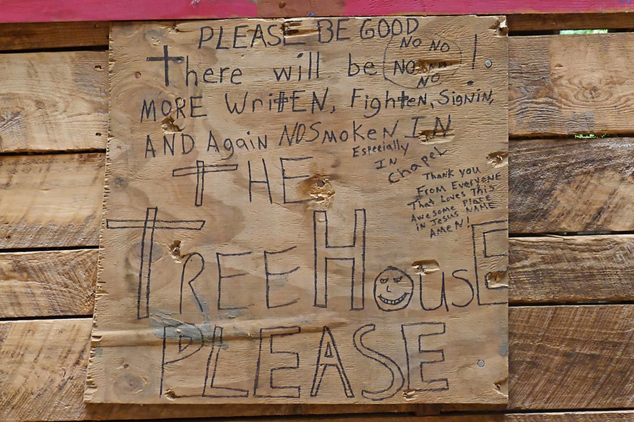 Holzschild mit der Aufschrift Bitte sei artig, es wird kein Schreiben, Kämpfen, Unterschreiben und kein Rauchen mehr geben, insbesondere im Baumhaus, bitte
