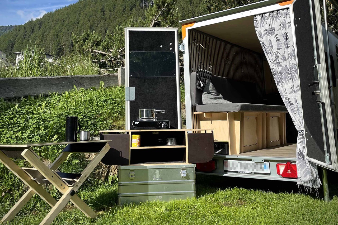 Campinganhänger mit Küche, Tisch und Stauraum im Freien.