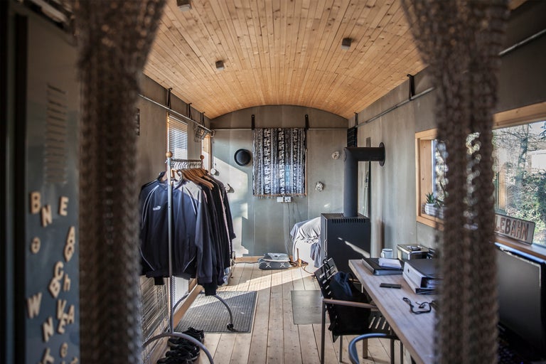 Innenansicht eines Arbeitszimmers mit Holzofen, Schreibtisch und Kleiderständer.