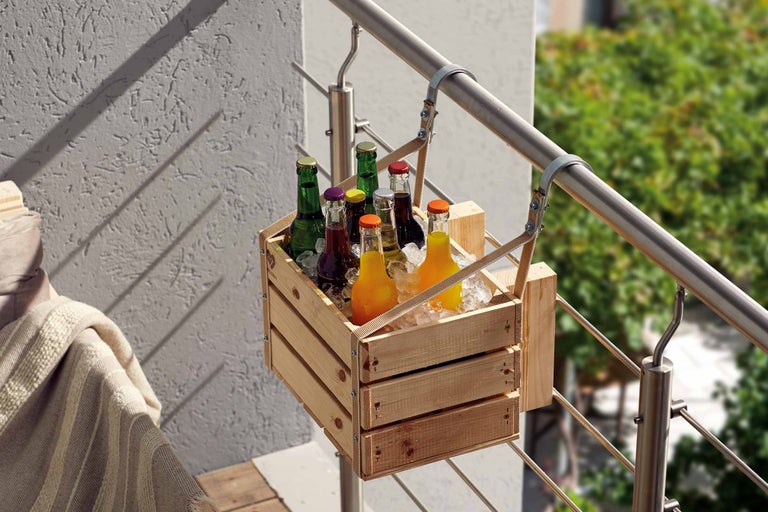Getränkekiste aus Holz, die mit Getränkeflaschen gefüllt ist, hängt an einem Geländer