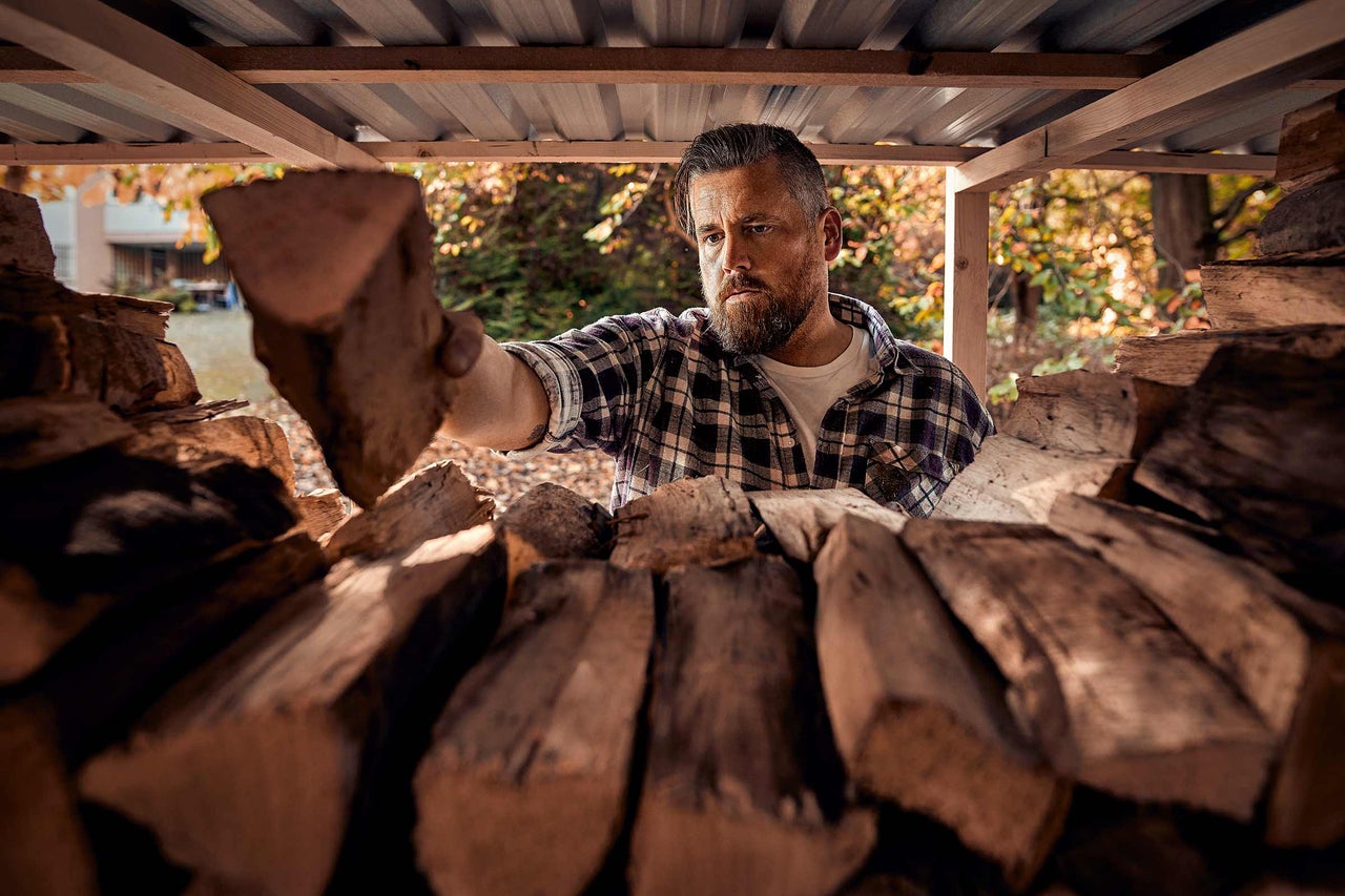 Mann lagert Brennholz in einem Holzschuppen.