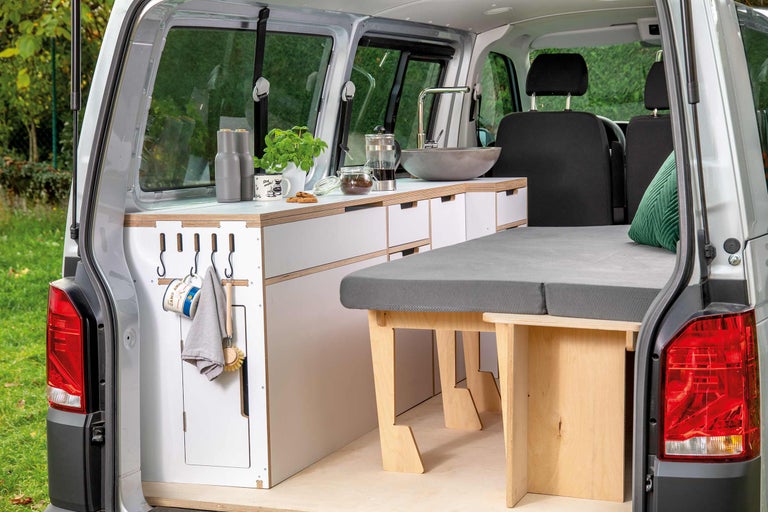 Innenraum eines Campingbusses mit Küchenzeile, Waschbecken, Schubladen und Bett