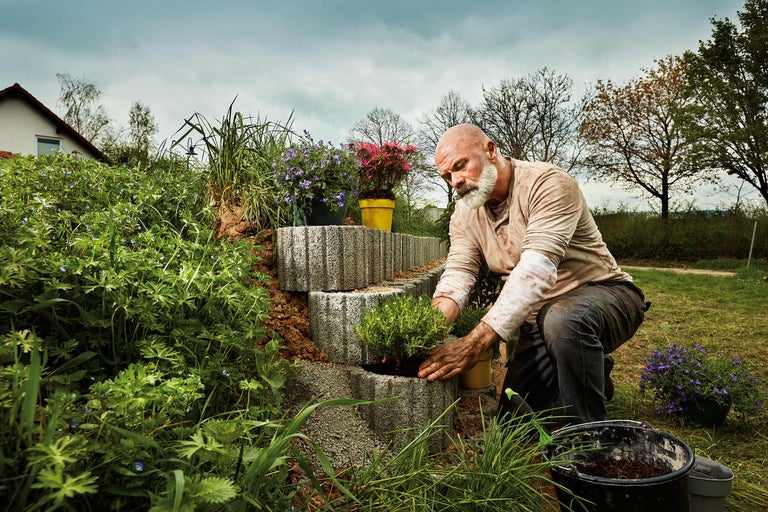 Ein Mann bepflanzt eine Gartentreppe aus Betonsteinen im Garten.