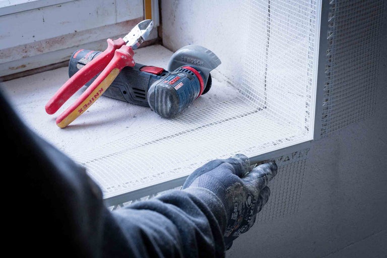 Installateur befestigt Armierungsgewebe, im Hintergrund Seitenschneider und Winkelschleifer