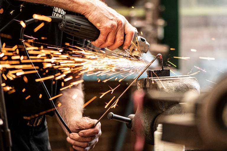 Eine Person schleift ein Metallstück mit einer Schleifmaschine, wobei Funken sprühen.