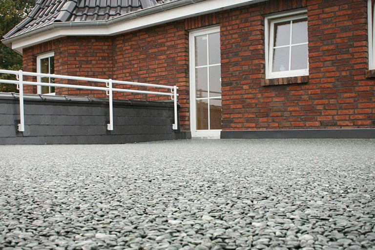 Dachterrasse mit Kies und Geländer vor einem Backsteingebäude