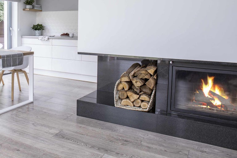 Kamin mit brennendem Holz und Holzkorb in einem hellen Wohnraum.