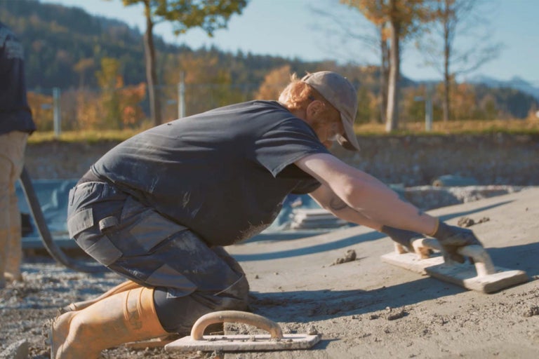Ein Bauarbeiter glättet eine Betonoberfläche mit einem Glättbrett.