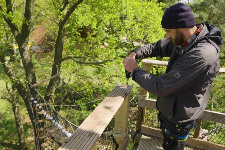 Mann arbeitet mit Bohrmaschine in einem Baumwipfelpfad