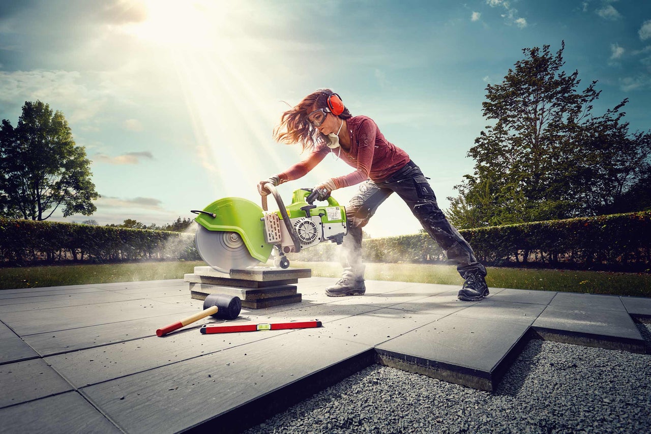 Frau schneidet Steinplatten mit einem Trennschleifer im Freien. Persönliche Schutzausrüstung wird verwendet.