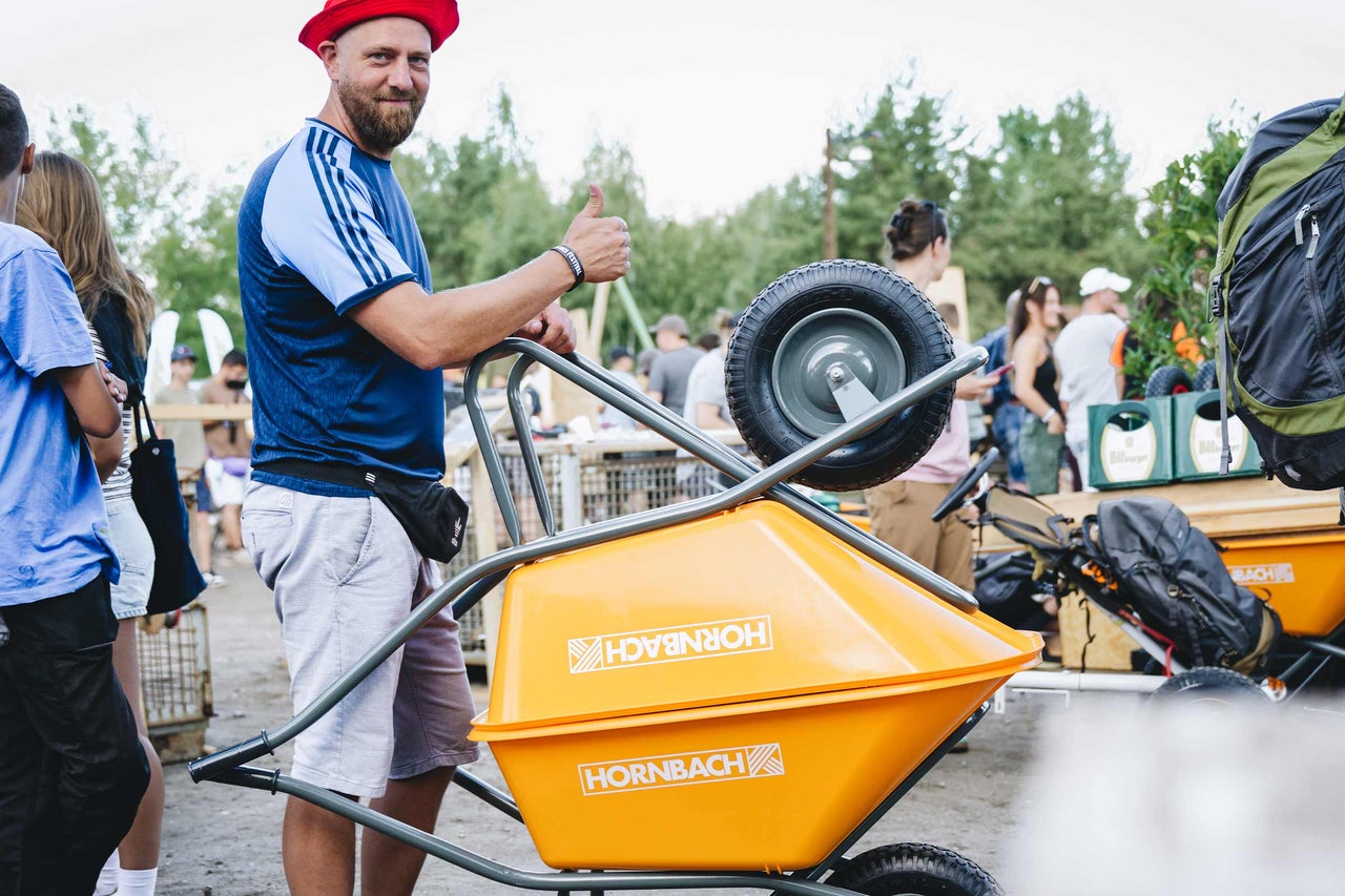 Ein Mann mit Hornbach Schubkarre bei einem Festival, er zeigt den Daumen nach oben.