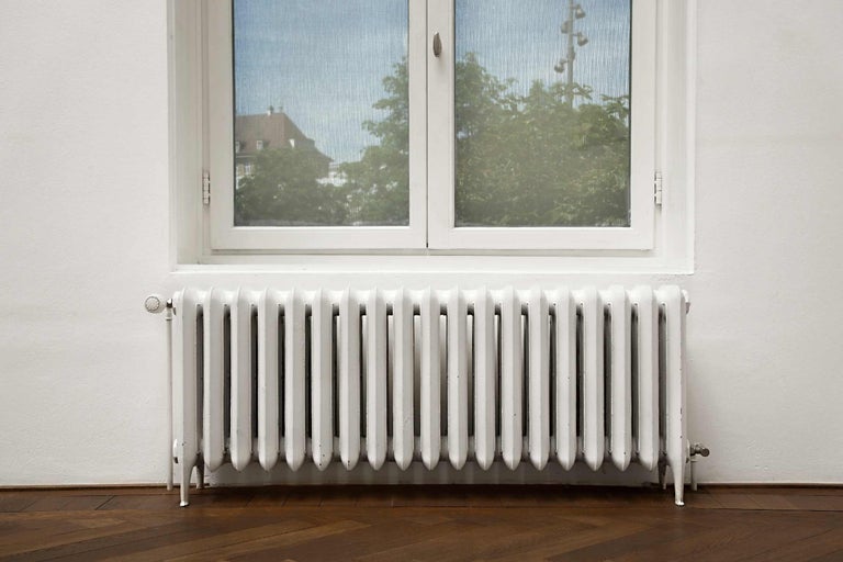 Weißer Heizkörper unter einem Fenster auf einem Holzboden