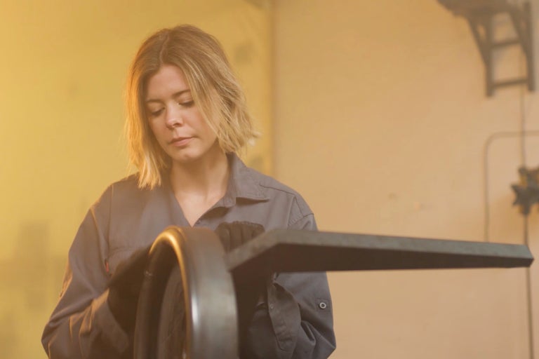 Frau in Arbeitskleidung bearbeitet Metallstück