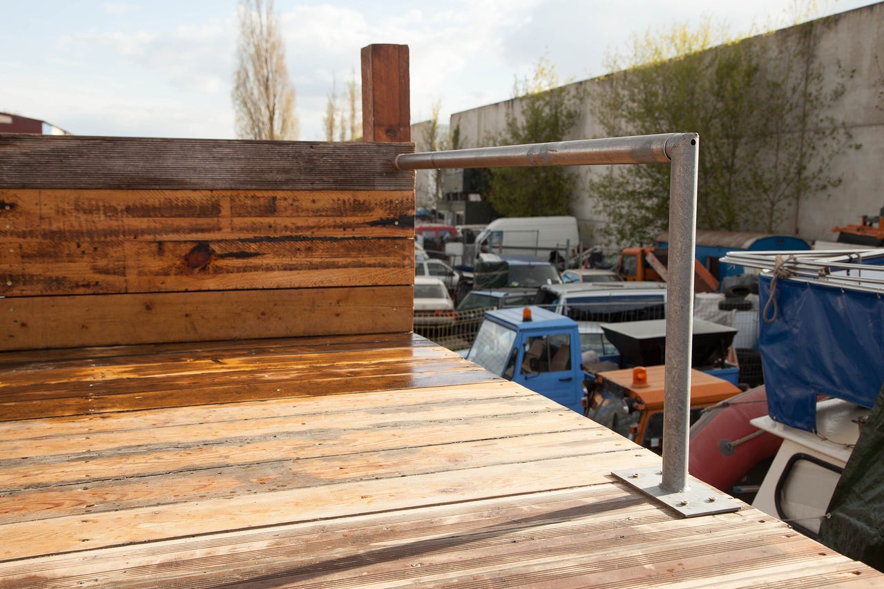 Holzdeck mit Metallgeländer und Fahrzeugen im Hintergrund