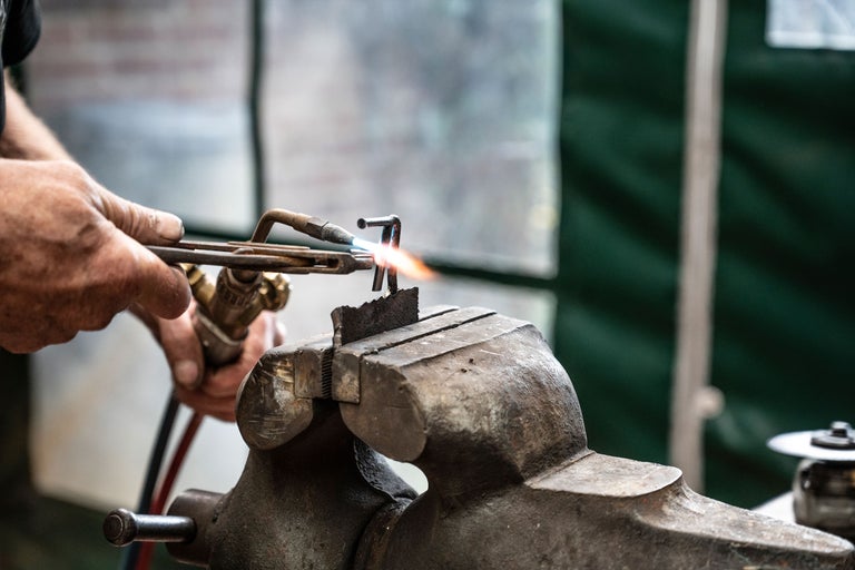 Ein Mann schweißt Metall mit einem Schweißbrenner, das in einem Schraubstock gehalten wird.