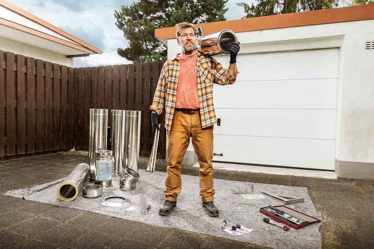 Mann mit Schornsteinbausatz im Freien unter leichtem Regen vor einer Garage