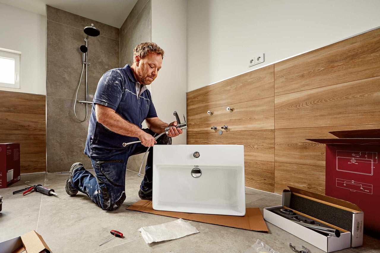 Ein Installateur montiert ein Waschbecken in einem Badezimmer mit Dusche.