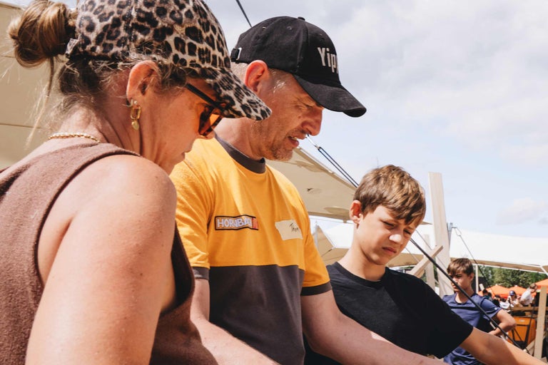 Ein Hornbach Mitarbeiter im gelb-grauen T-Shirt berät eine Kundin und einen Jugendlichen bei einem Projekt im Außenbereich.