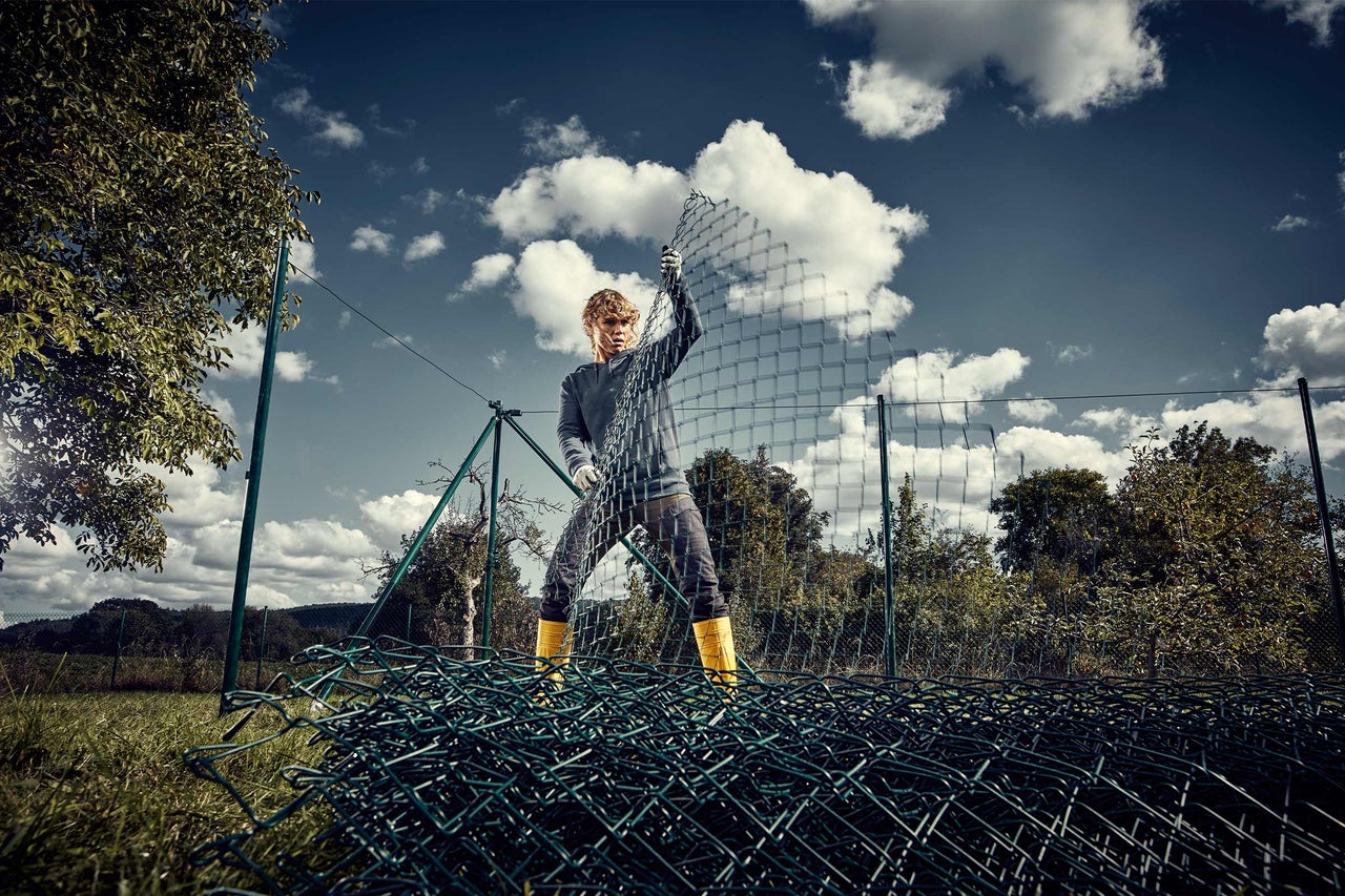 Eine Person installiert einen Maschendrahtzaun im Garten.