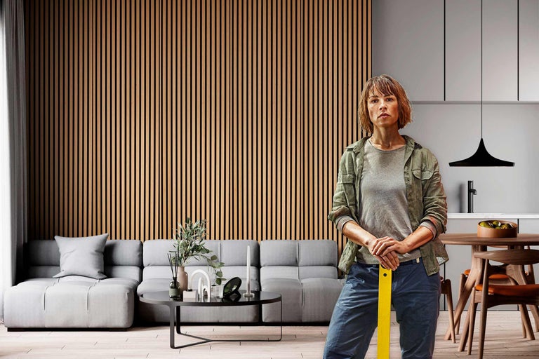 Wohnzimmer mit Akustikpaneelen an der Wand, grauer Couch und einer Frau im Vordergrund