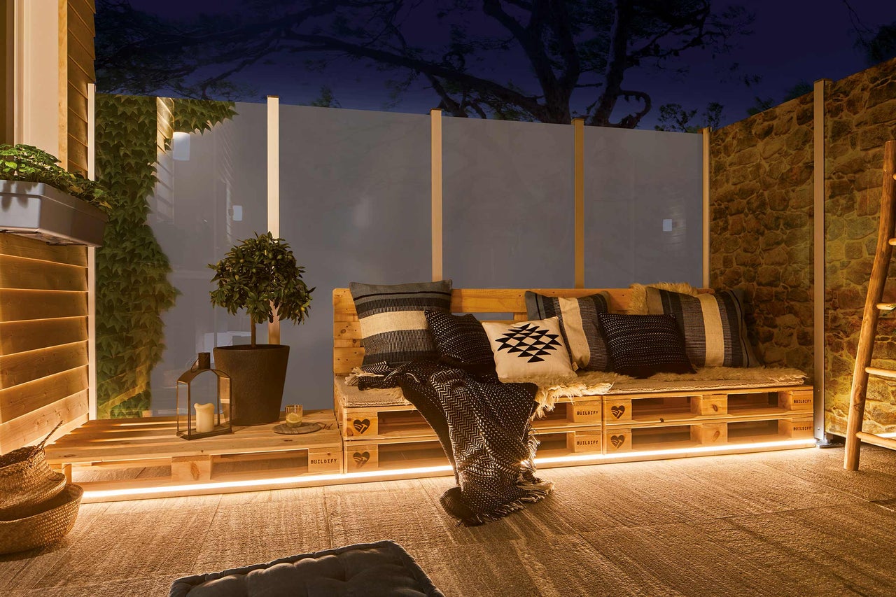 Gestaltete Terrasse mit Holzmöbeln, Pflanzen und dekorativer Beleuchtung für eine gemütliche Atmosphäre im Freien.