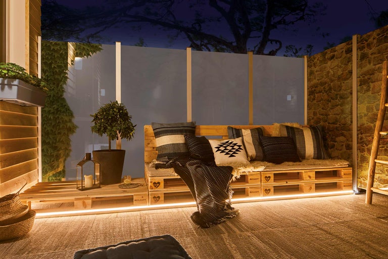 Gestaltete Terrasse mit Holzmöbeln, Pflanzen und dekorativer Beleuchtung für eine gemütliche Atmosphäre im Freien.