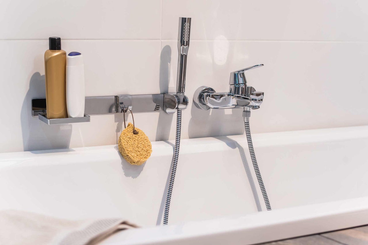 Badezimmerarmatur mit Handbrause, Duschgel und Badeschwamm an einer Badewanne