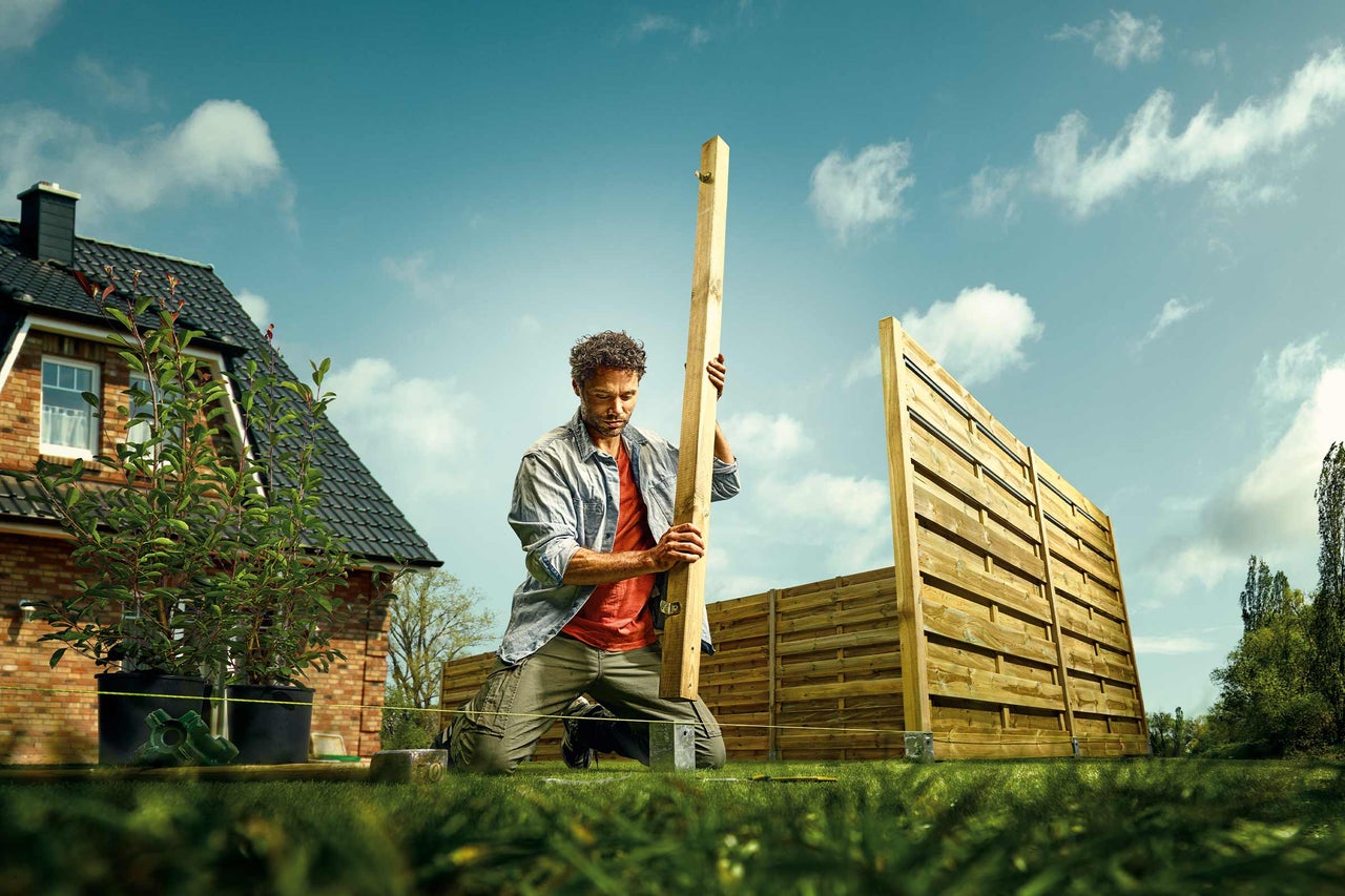 Mann kniet beim Aufbau eines Gartenzauns aus Holz