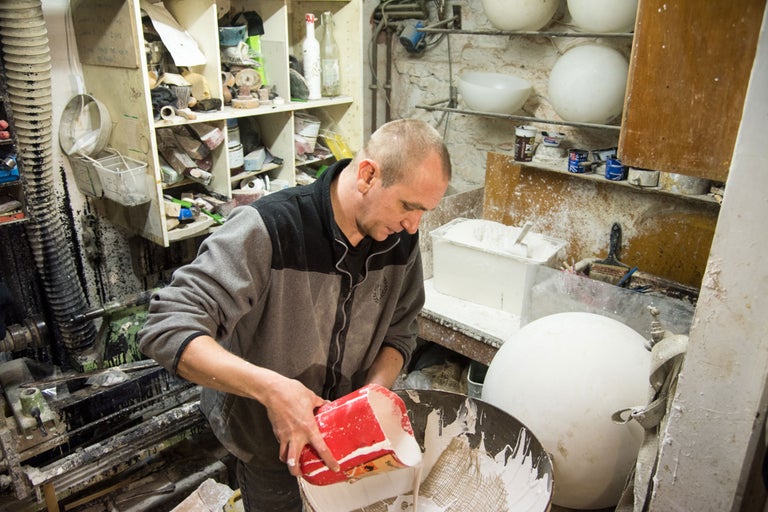 Mann gießt Flüssigkeit aus einem Behälter in eine Wanne in einer Werkstatt.
