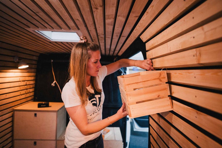 Frau montiert eine Holzkiste an einer Wand aus Holzpaneelen in einem Campervan.