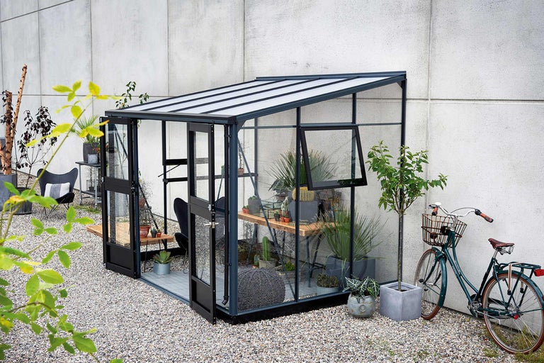 Gewächshaus mit Pflanzen und Gartendekoration im Außenbereich.