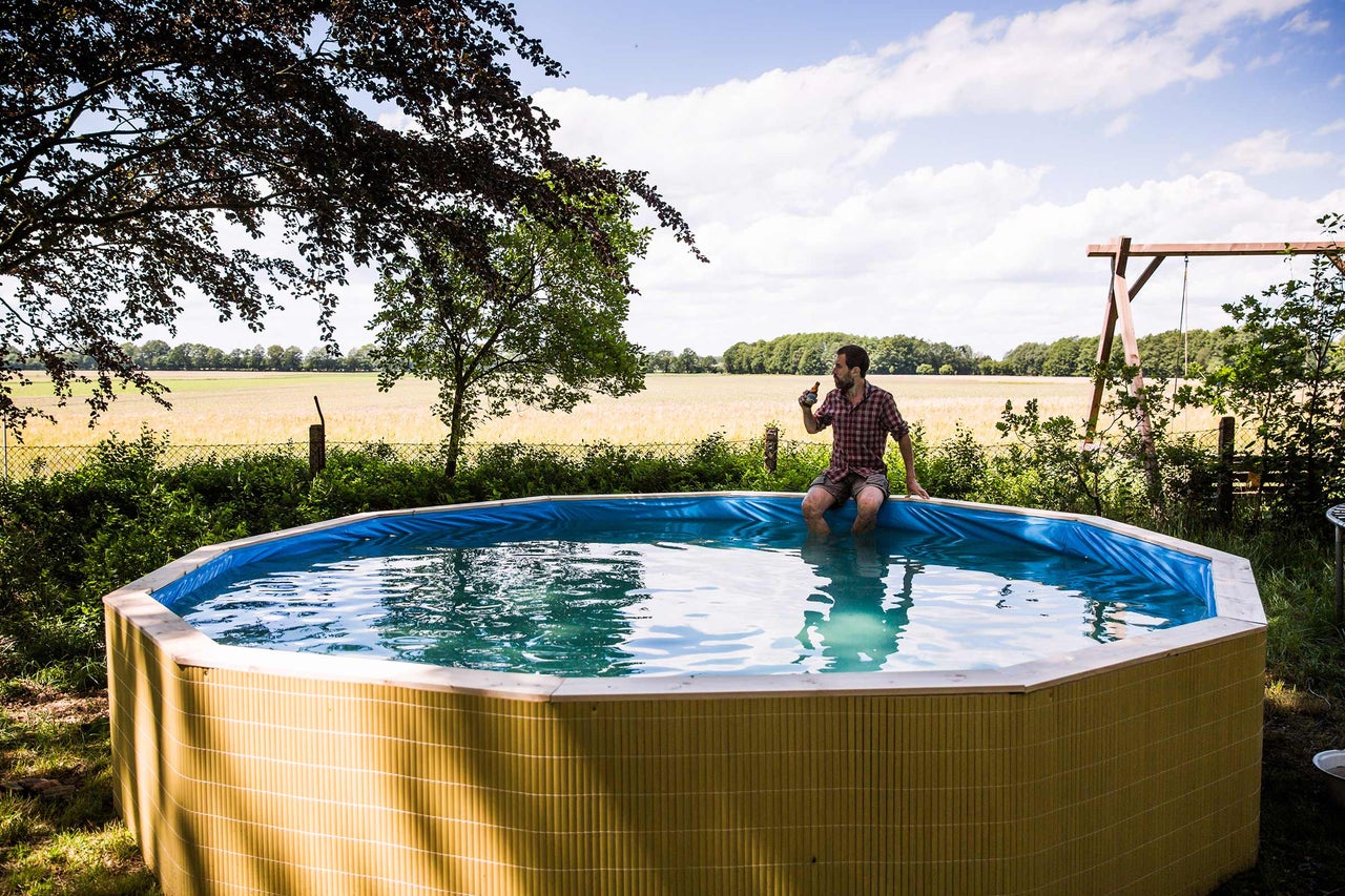 Mann sitzt mit einem Getränk auf einem Pool im Garten.